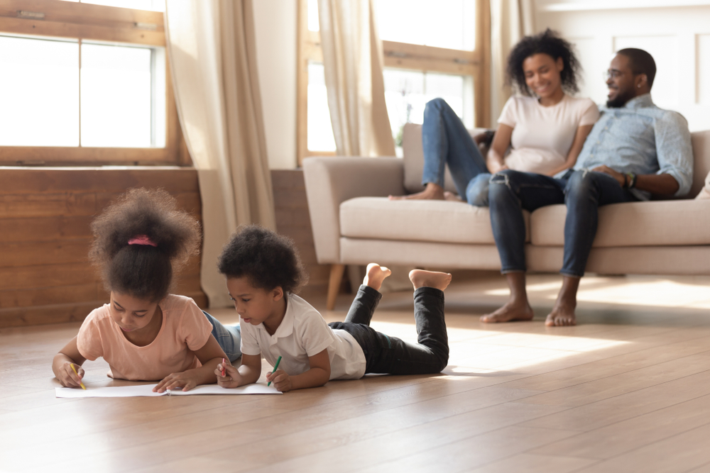 Two children cooler on the floor while the parents watch from the couch. 