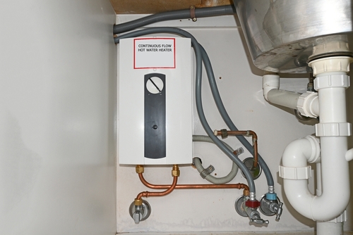 A tankless water heater mounted beneath a kitchen counter.